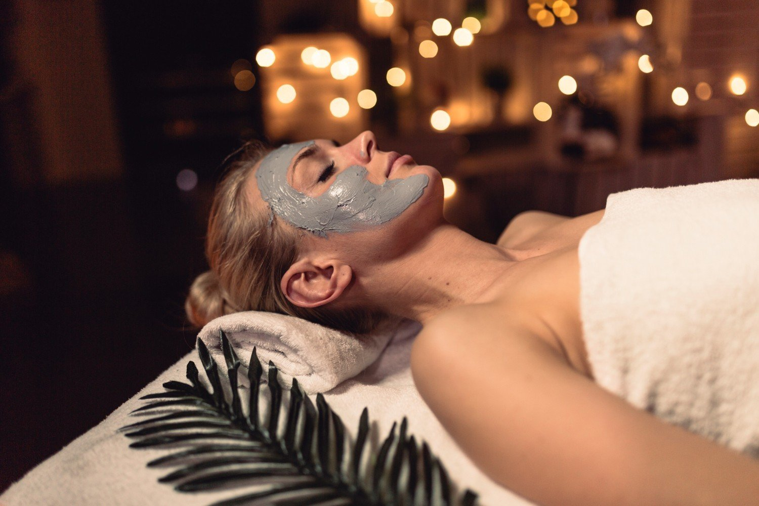 Vrouw ontspannen met gezichtsmasker in een sfeervolle spa-omgeving met zachte verlichting